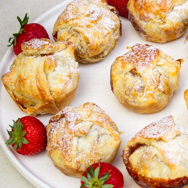 mini apple pies dusted with powdered sugar on plate with strawberries.