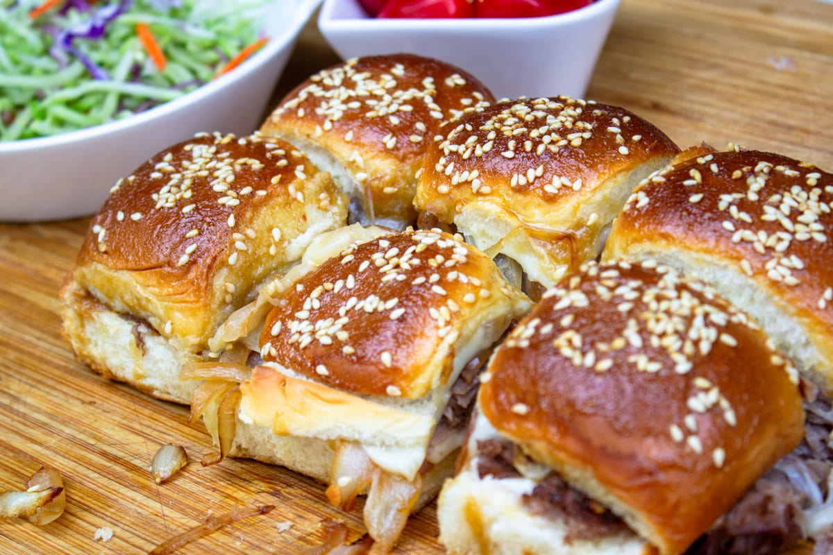 baked beef sliders on cutting board with slaw and tomatoes.