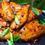 glazed chicken wings on black plate with green onion garnish.