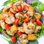 grilled shirmp panzanella with pesto on greens on a plate.
