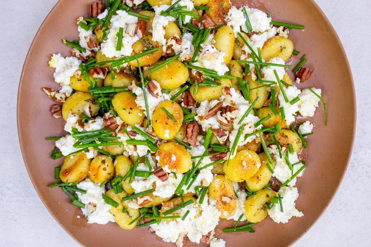 Pan-fried gnocchi with lemon ricotta, nuts and chives on plate.