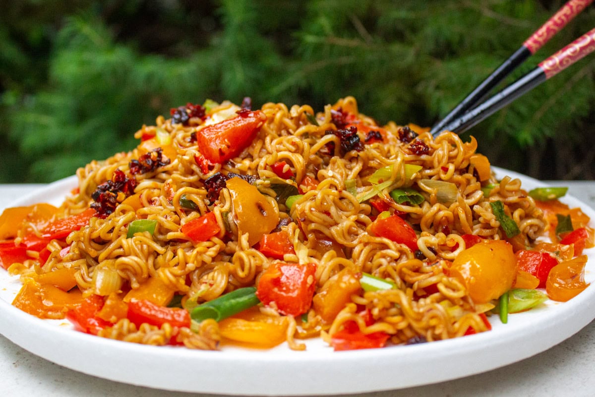 Spicy ramen noodles with veggies on plate with chop sticks.