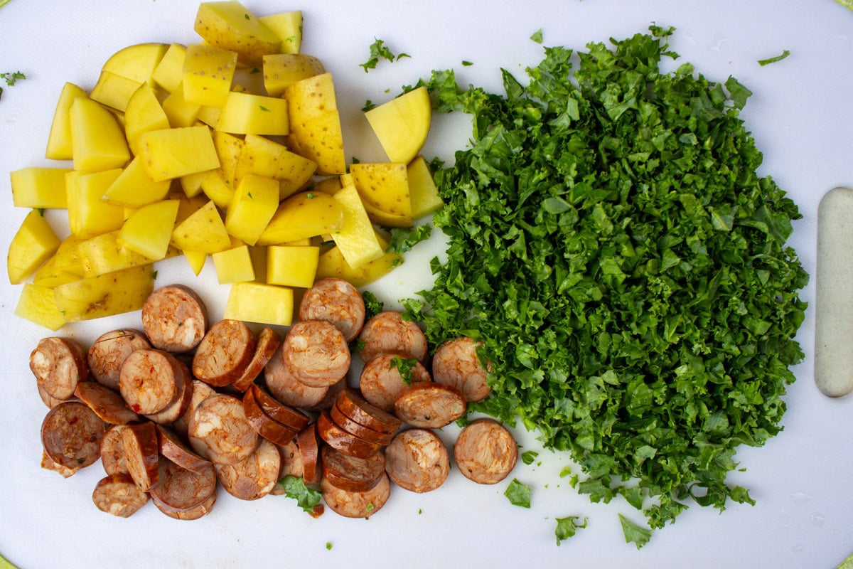 Finely chopped kale, diced potatoes and sliced cooked sausage on cutting board.