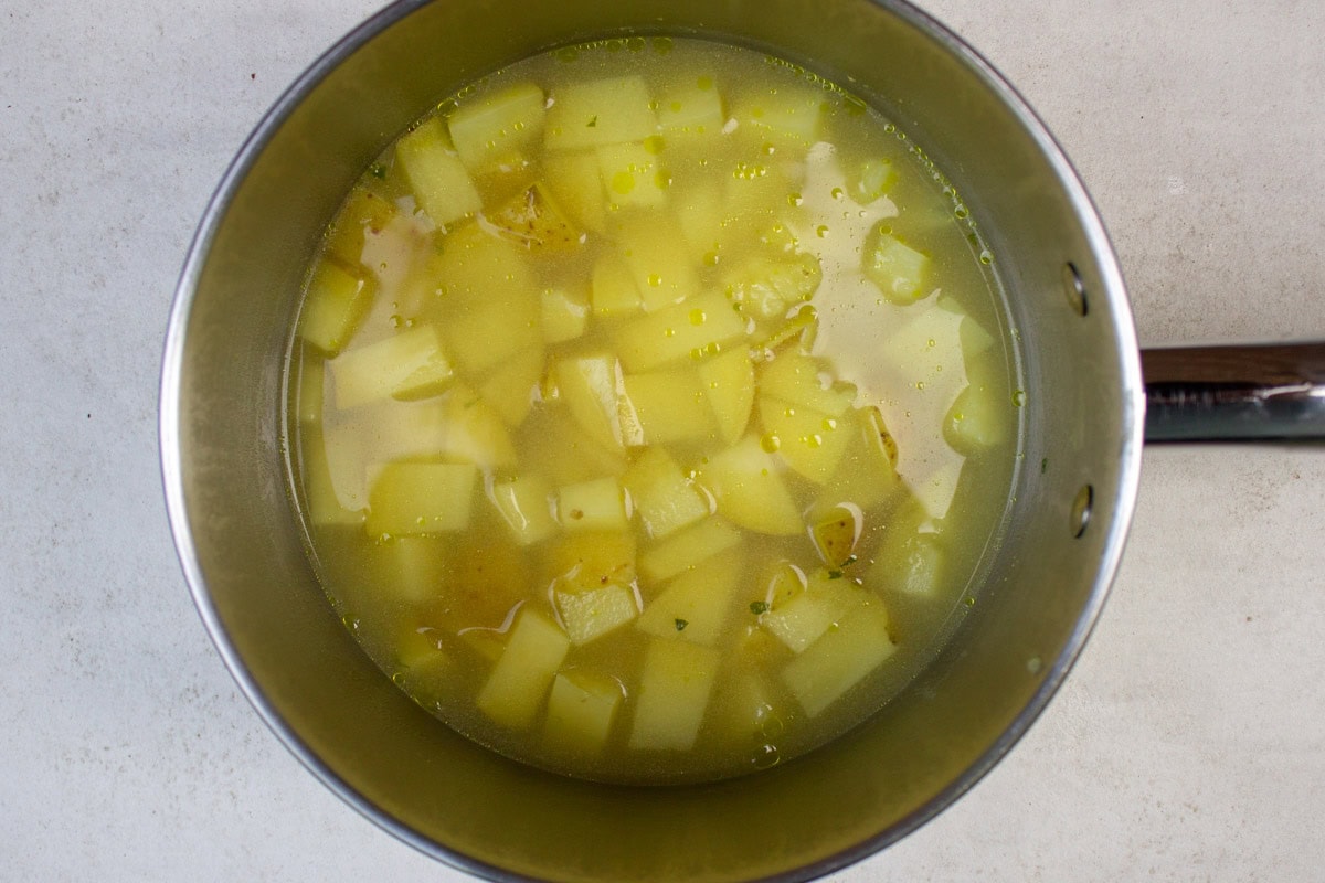 Cooked potato chunks in chicken broth in a pot.