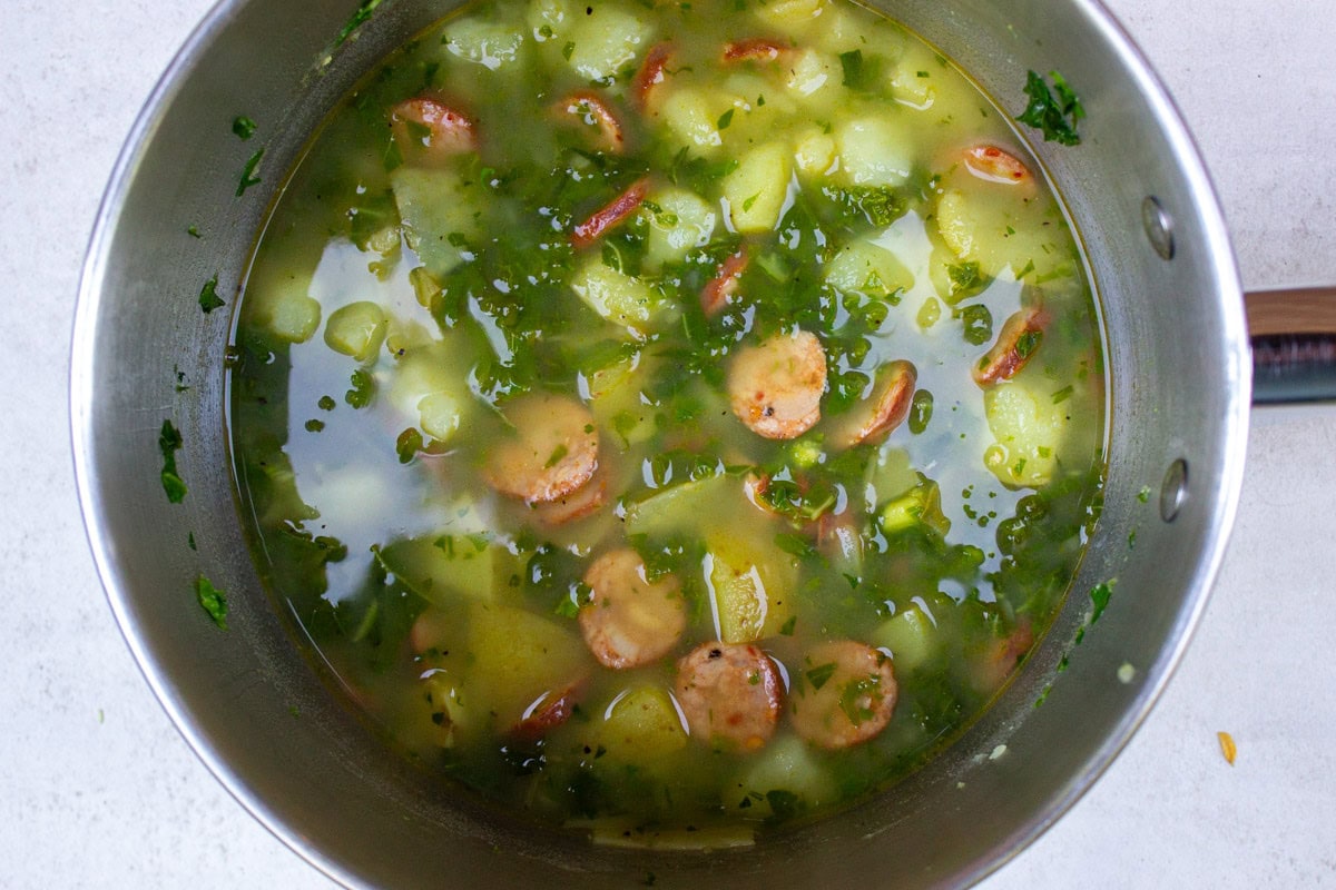 Pot of soup with kale, potato chunks and sausage disks.