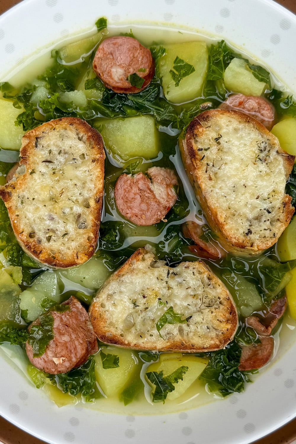 Bowl of soup with kale, potato chunks and sausage disks.