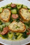 Bowl of soup with kale, potato chunks and sausage disks.