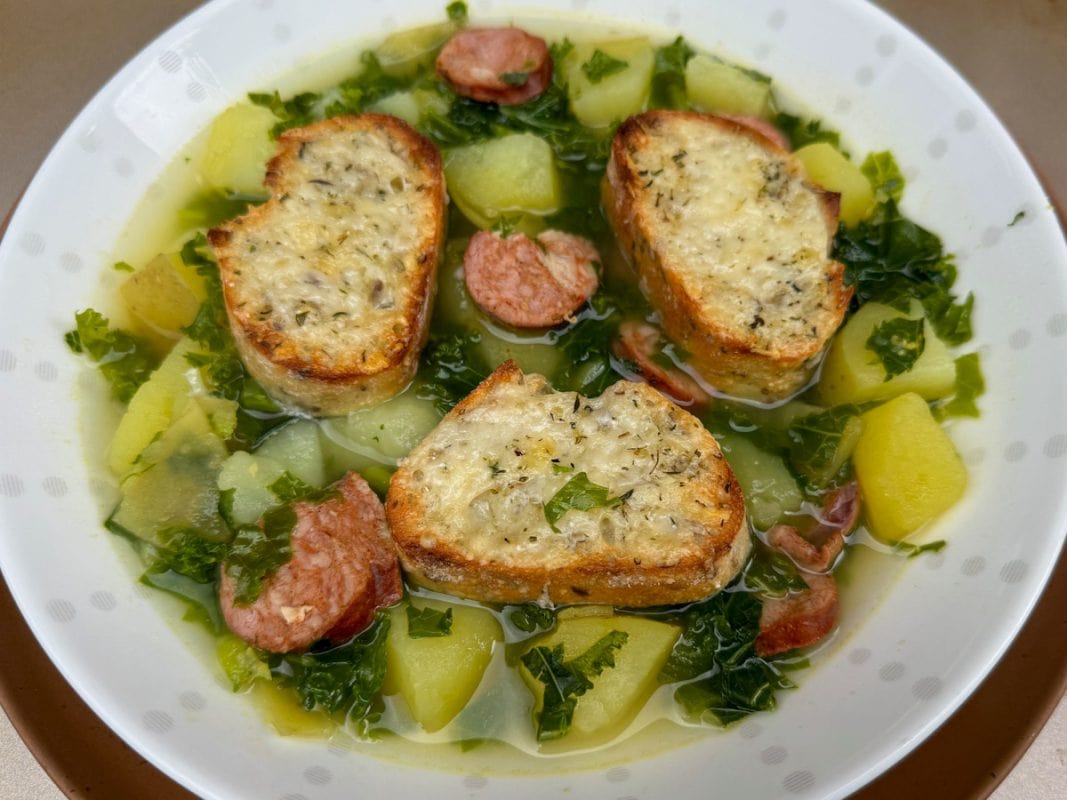 Bowl of soup with kale, potato chunks and sausage disks.