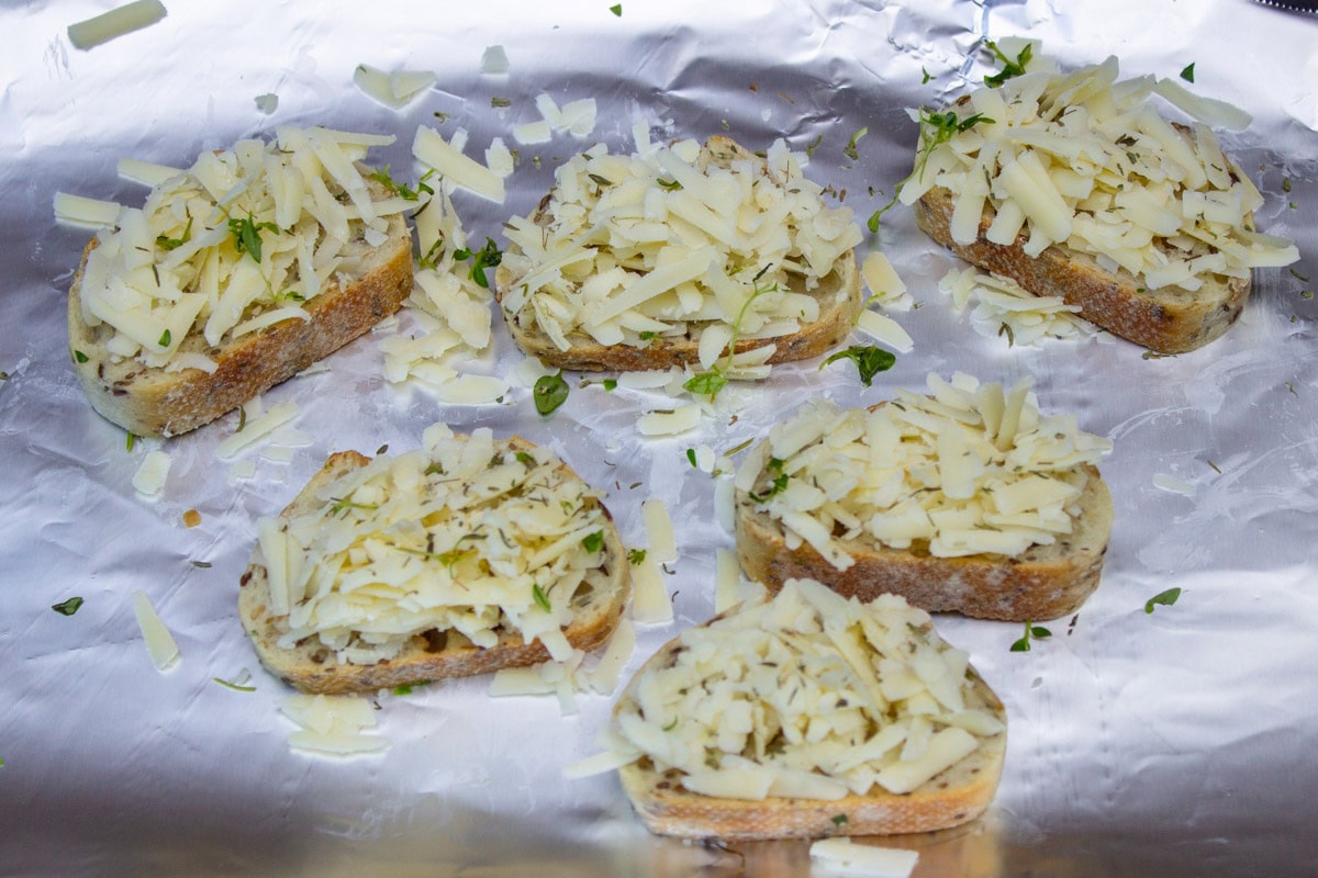 Cheese on baguette slices on foil on pan.