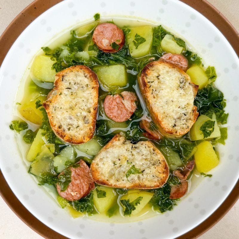 Bowl of soup with kale, potato chunks and sausage disks.