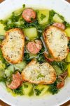 Bowl of soup with kale, potato chunks and sausage disks.