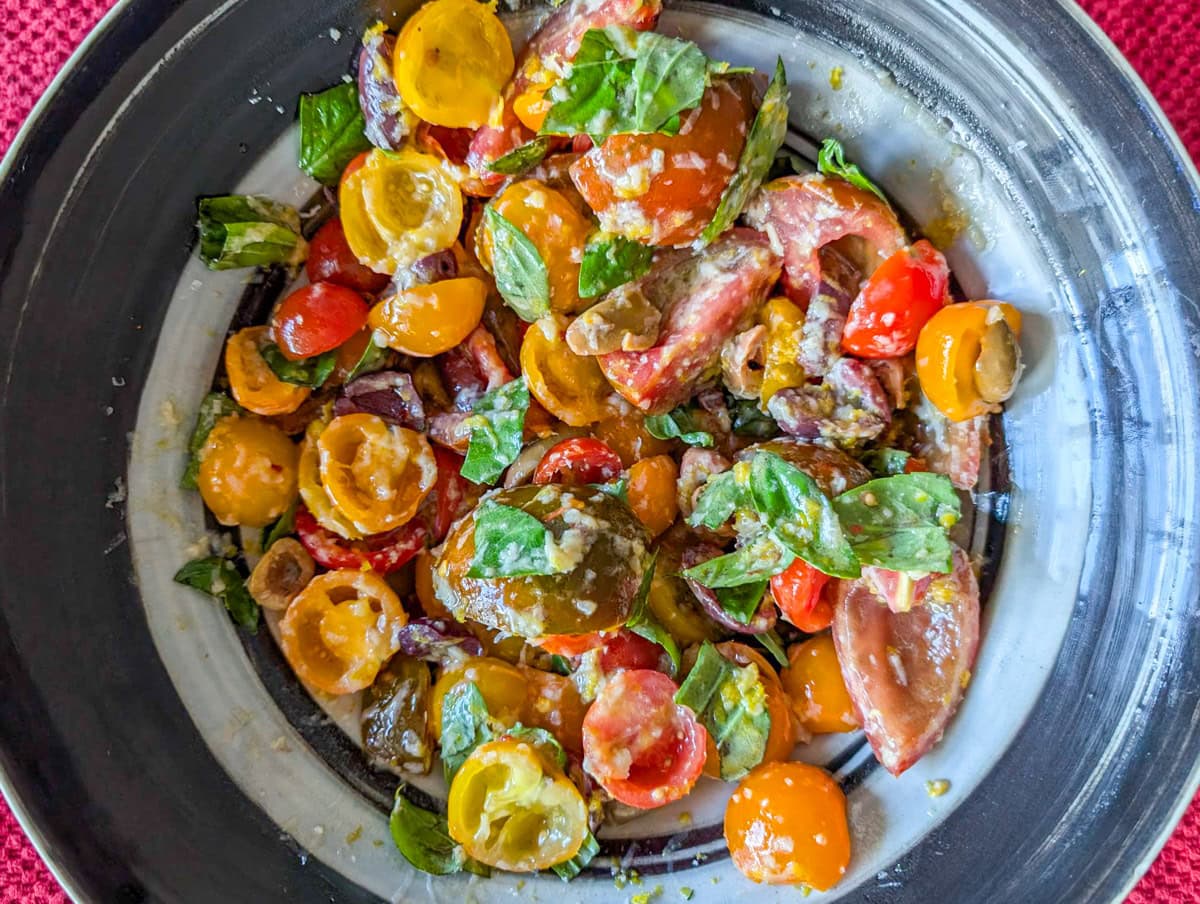 Tomatoes, basil and lemon with dressing mixture in a bowl.