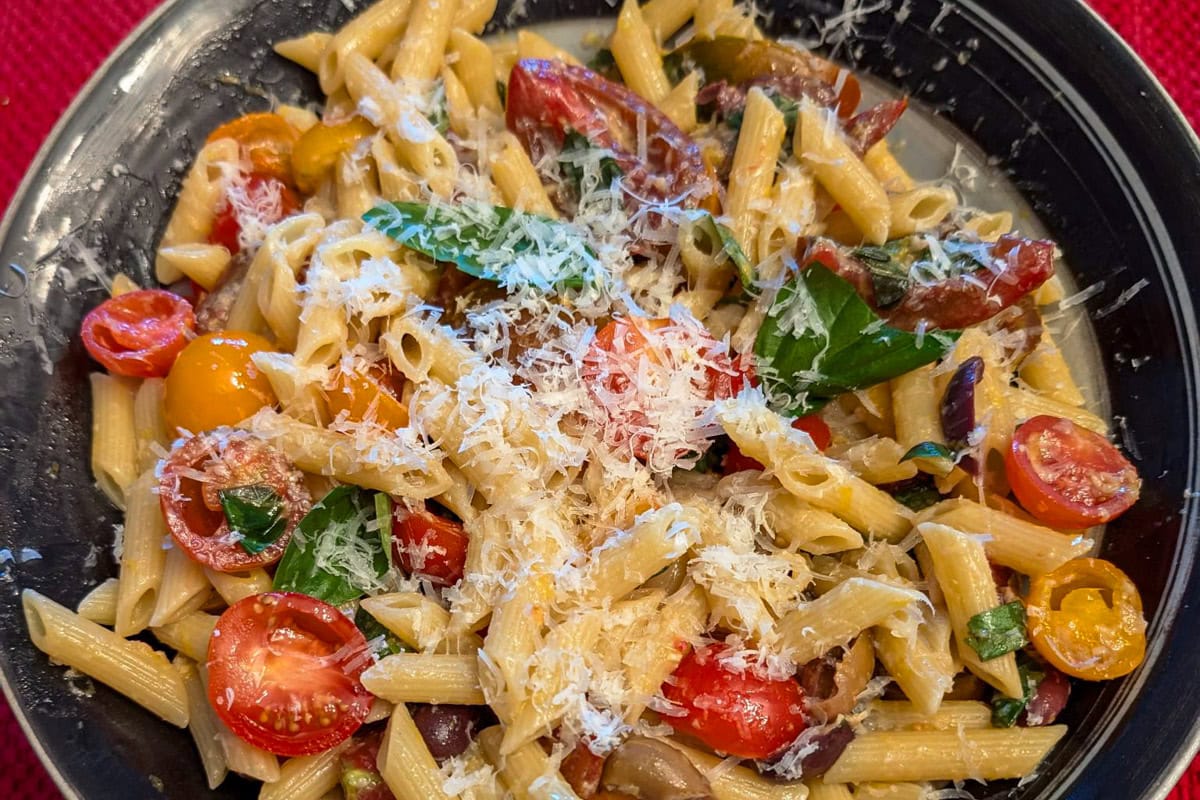 Serving bowl of tomato and basil pasta topped with parmesan cheese.