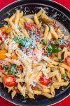 Serving bowl of tomato and basil pasta topped with parmesan cheese.