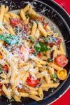 Serving bowl of tomato and basil pasta topped with parmesan cheese.