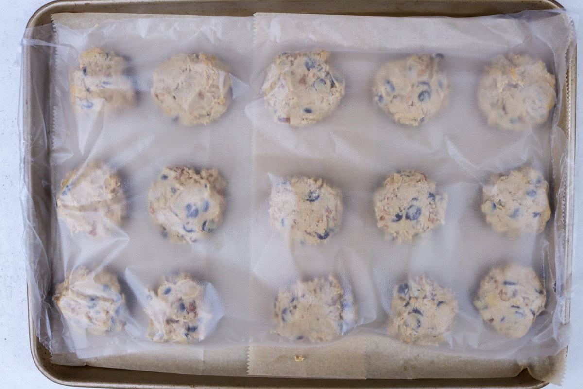 Cookie dough balls on baking sheet, covered with plastic wrap for chilling.