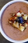 A bowl of chocolate mousse topped with diced apple, toasted nuts, chocolate shavings and blueberries.