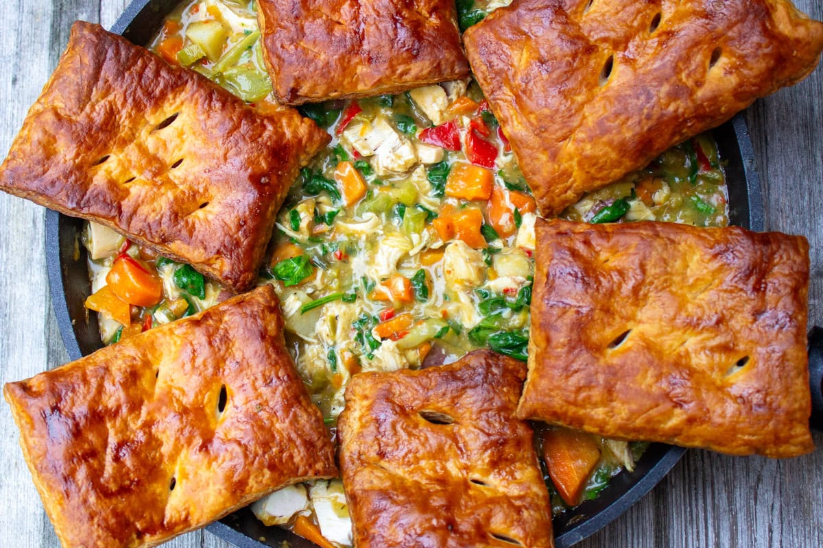 Chicken pot pie filling topped with puff pastry squares in a skillet.