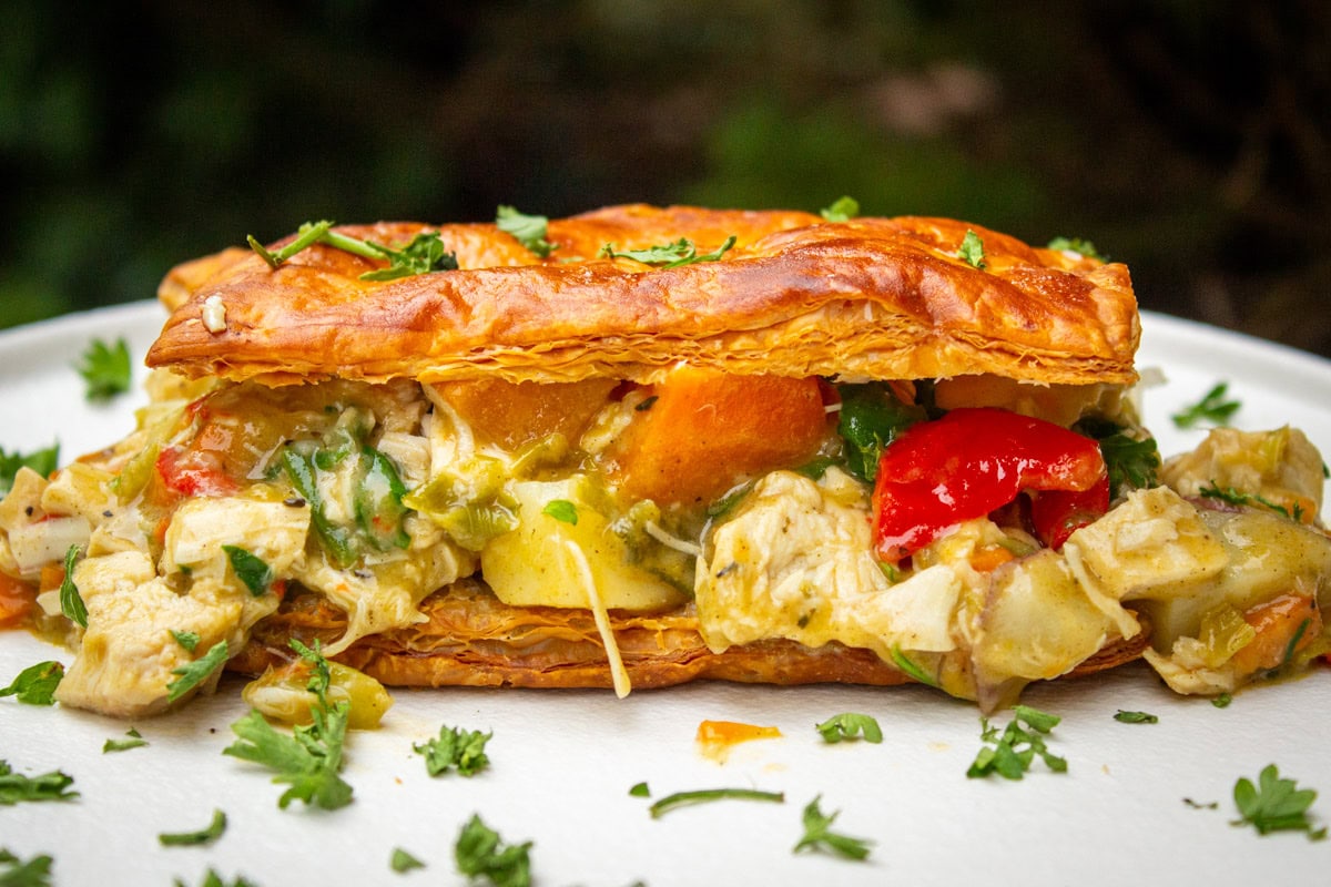 Chicken pot pie filling between two puff pastry squares on plate.