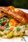 Chicken pot pie filling topped with puff pastry squares on a plate.