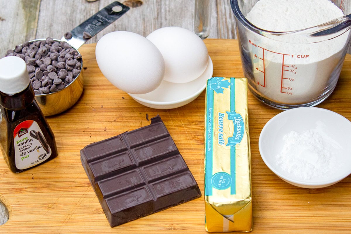 Eggs, unsweetened dark chocolate, sugar, chocolate chips, butter, flour, baking powder on cutting board. 