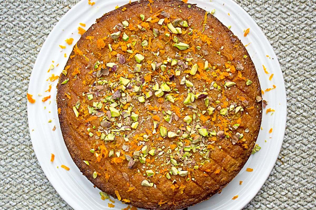 Garnished orange polenta cake on white plate.