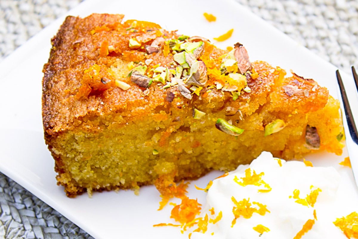 Piece of orange polenta cake with whipped cream beside it on plate.