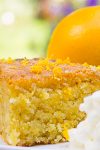 Piece of orange polenta cake with whipped cream and whole orange beside it on plate.