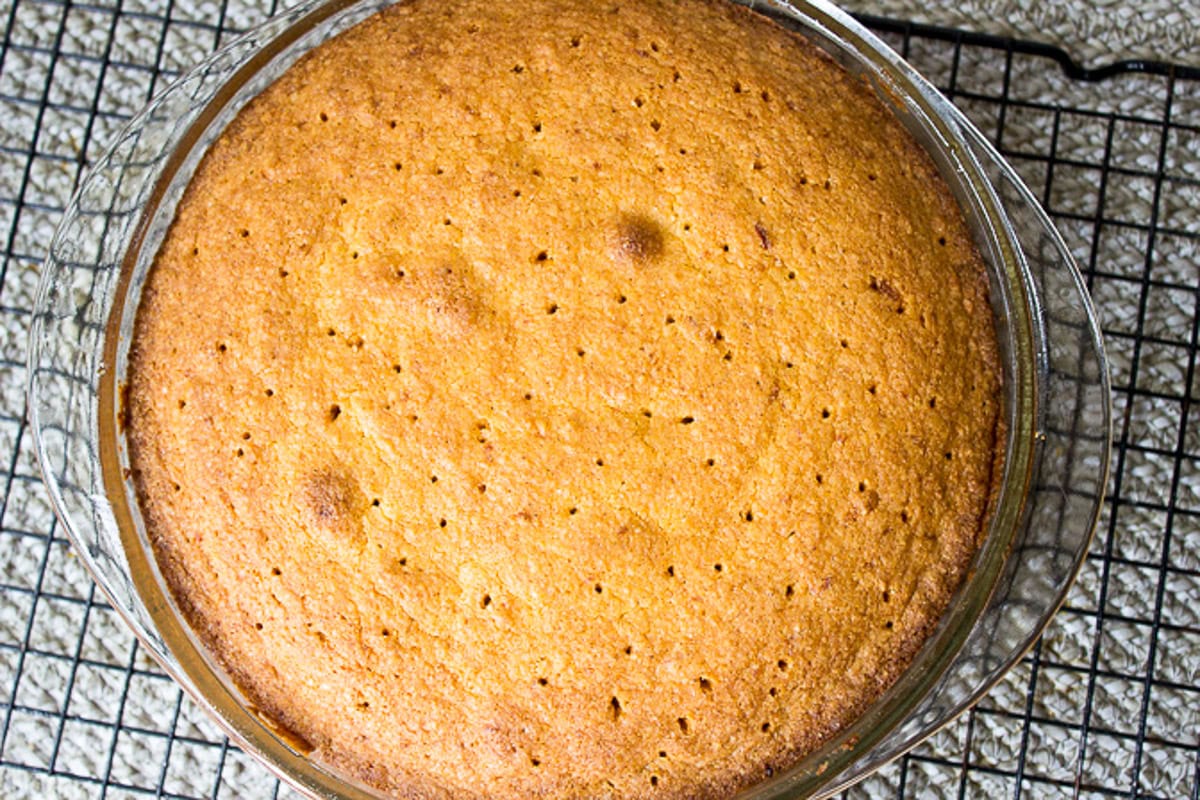 Baked polenta cake with tiny holes poked on top in cake pan.