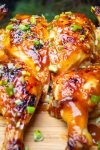 Glazed butterflied teriyaki chicken on cutting board garnished with chopped green onions.