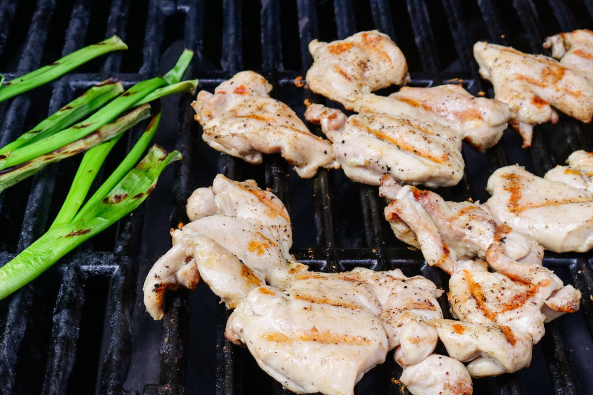 Boneless chicken on the grill with green onions.