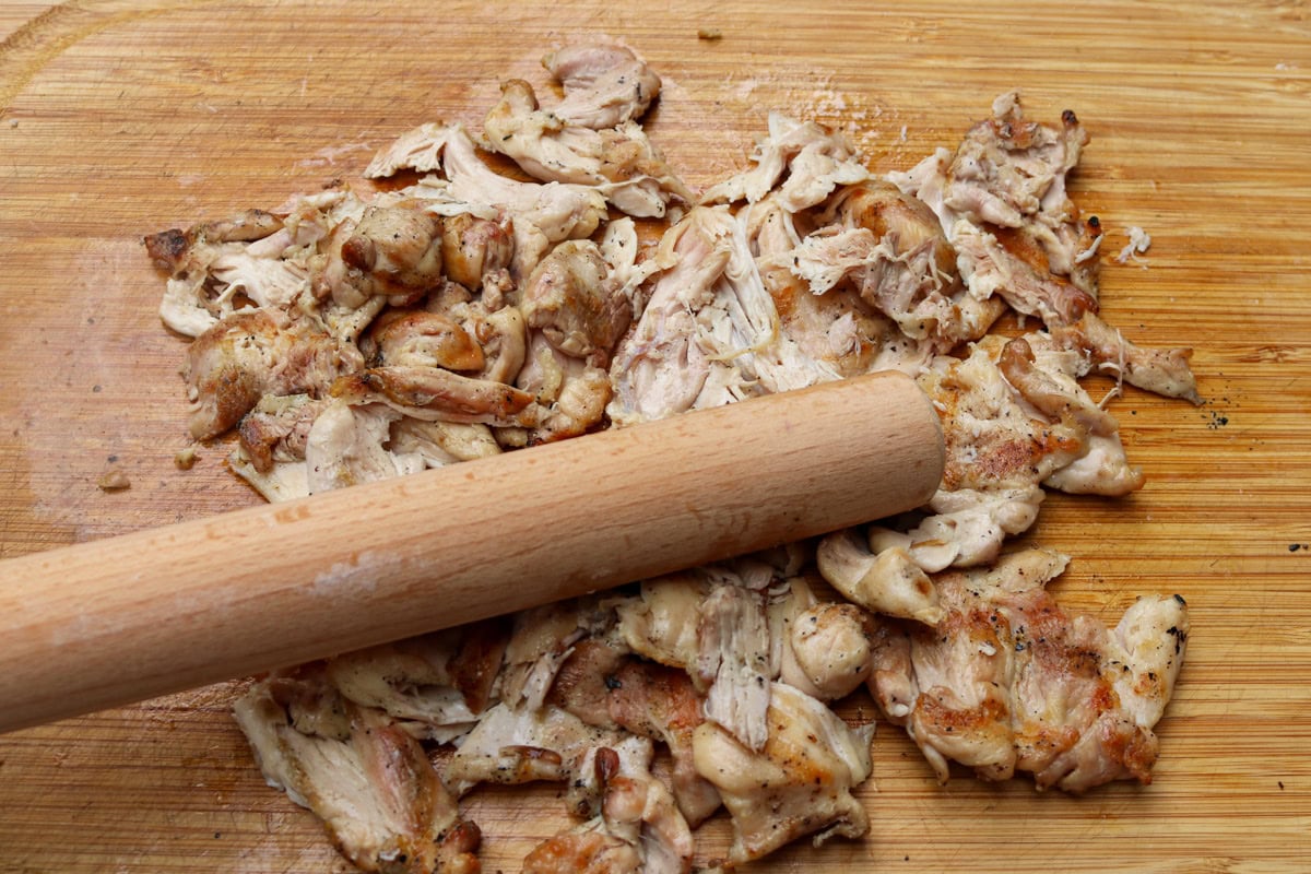 Shredded chicken with rolling pin on cutting board.