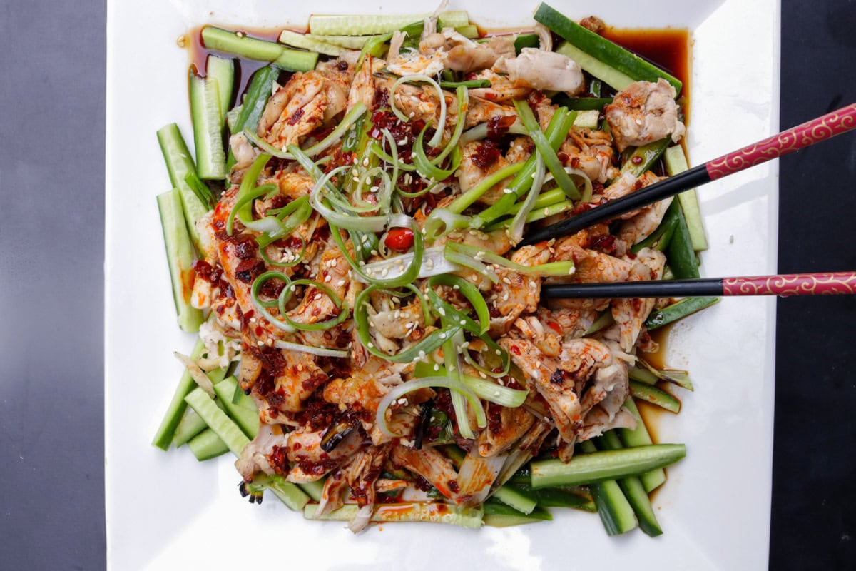 Bang bang chicken served over matchstick cucumbers and garnished with green onions on a plate.