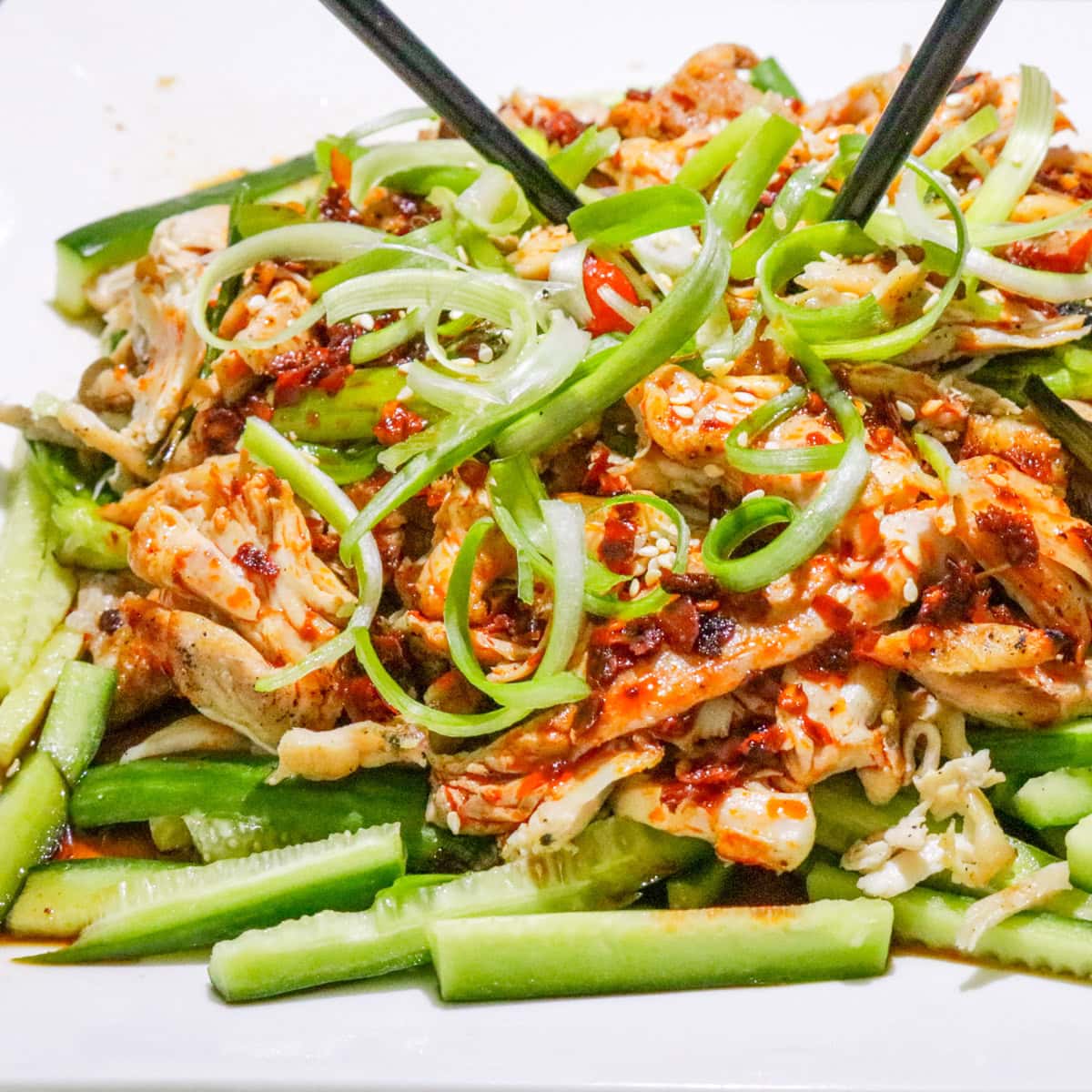 Bang bang chicken served over matchstick cucumbers and garnished with green onions on a plate.