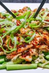 Bang bang chicken served over matchstick cucumbers and garnished with green onions on a plate.