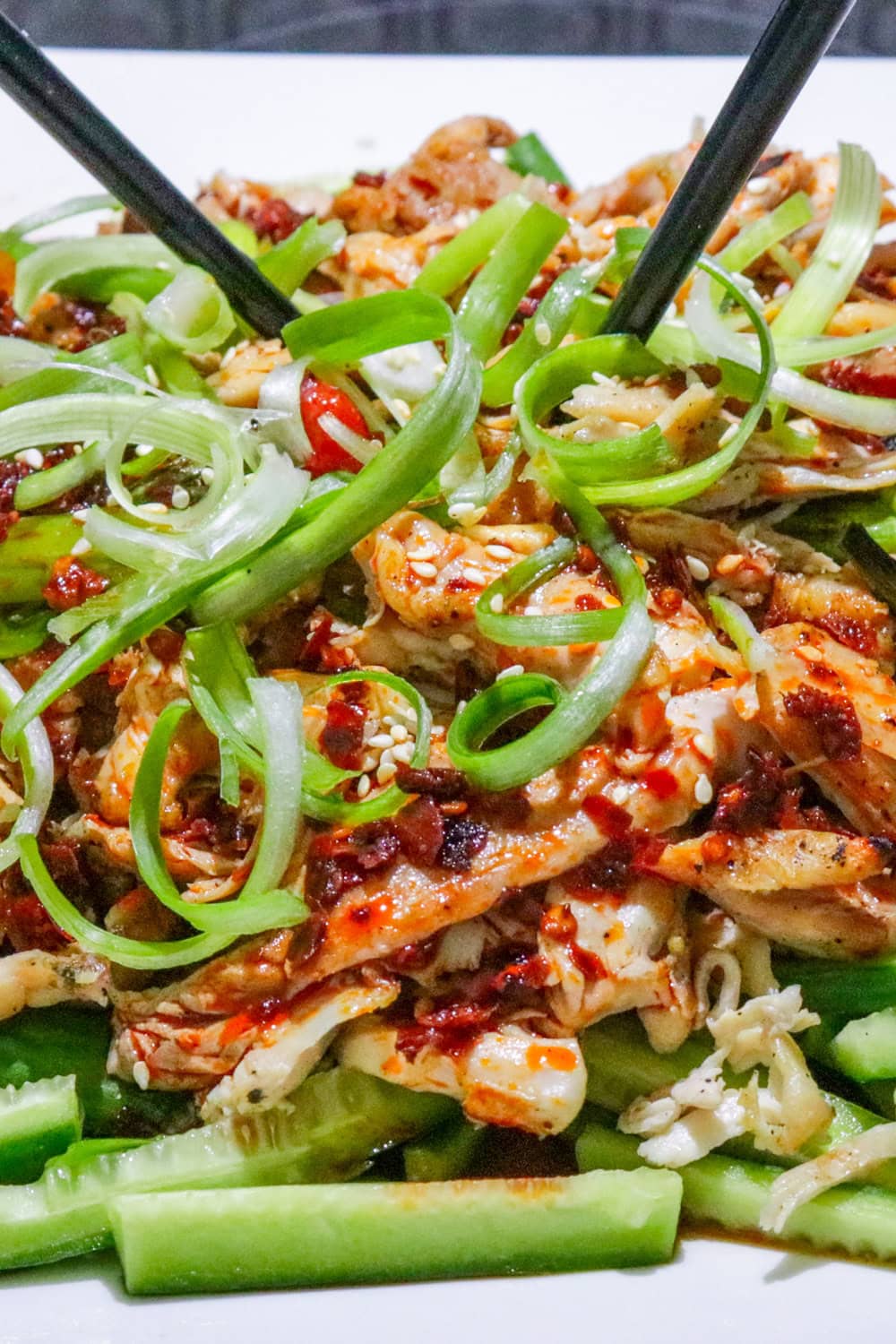Bang bang chicken served over matchstick cucumbers and garnished with green onions on a plate.