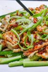 Bang bang chicken served over matchstick cucumbers and garnished with green onions on a plate.