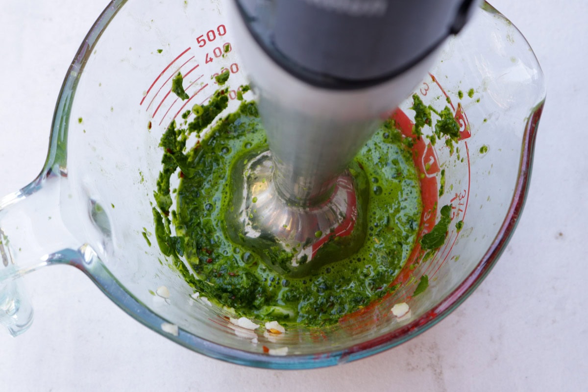 Chimichurri sauce in measuring cup with immersion blender.