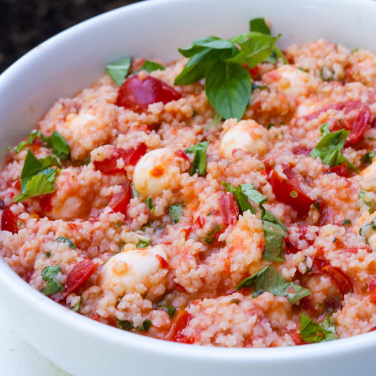Pastina salad caprese style in a white bowl with basil.