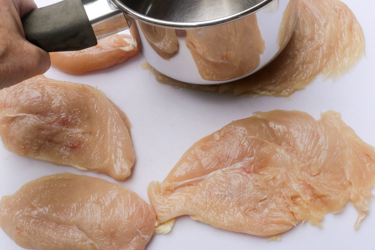 Split chicken breast halves being pounded with bottom of small saucepan.