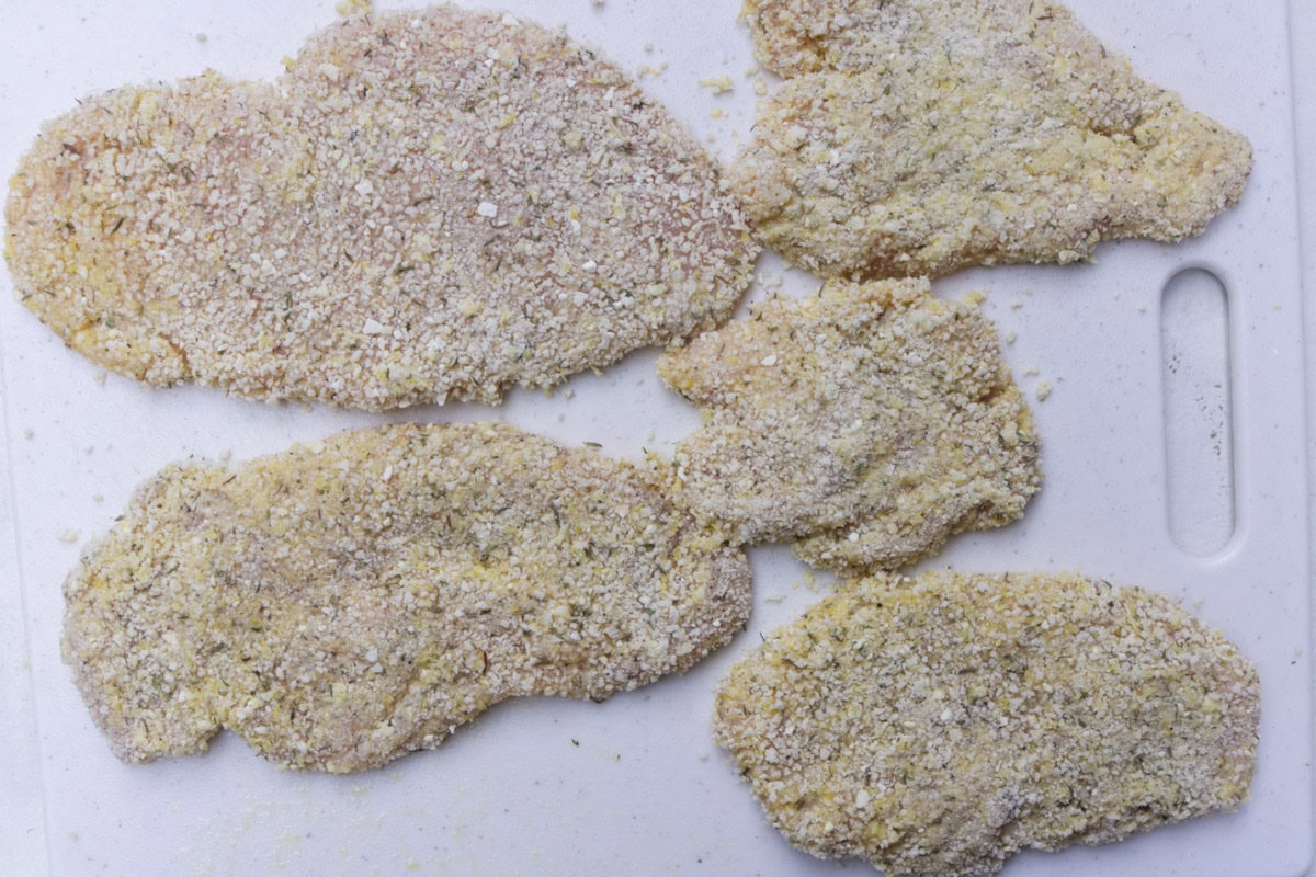 Breaded raw chicken cutlets on cutting board.