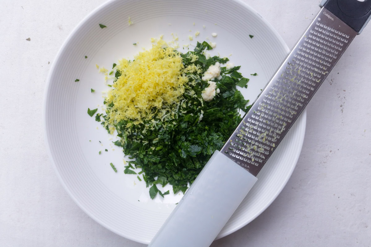 Chopped parsley, lemon zest and minced garlic in bowl with microplane at the side.