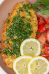 Breaded Italian chicken cutlet with gremolata, tomato salad and lemon slices on plate.
