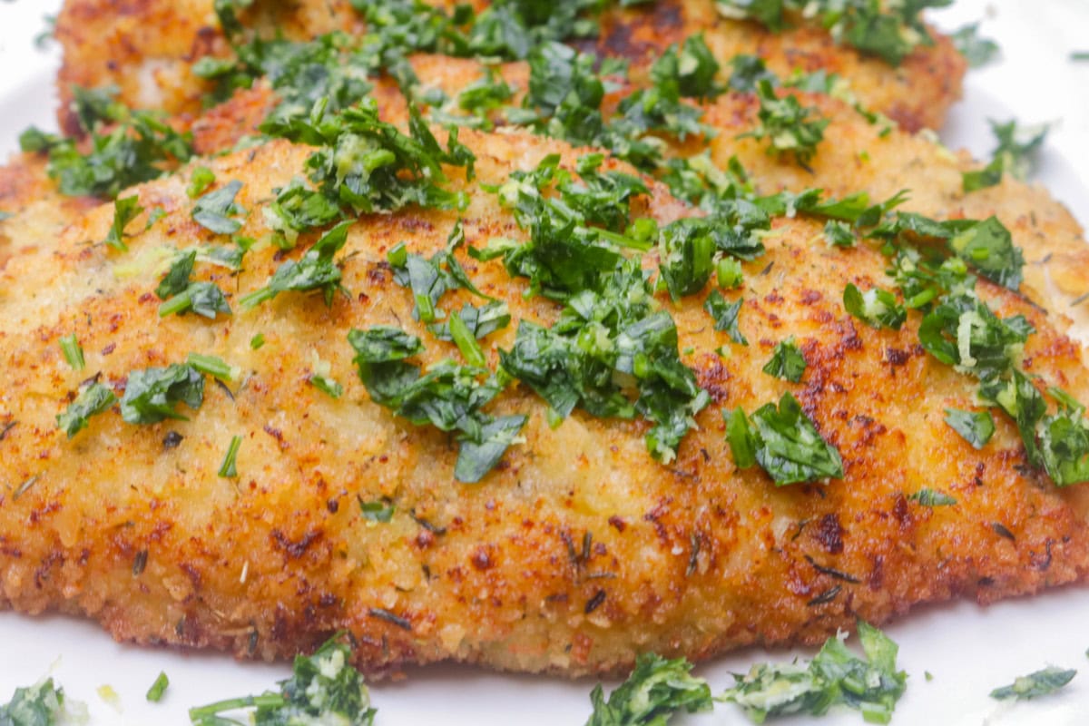 One crispy chicken cutlet with gremolata on plate.