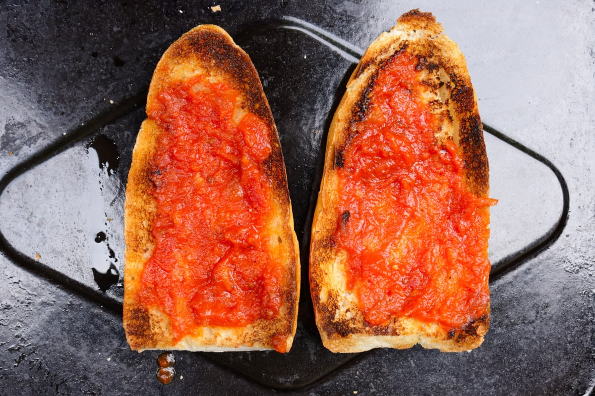 One split toasted roll with tomato sauce on each half sitting on tray.