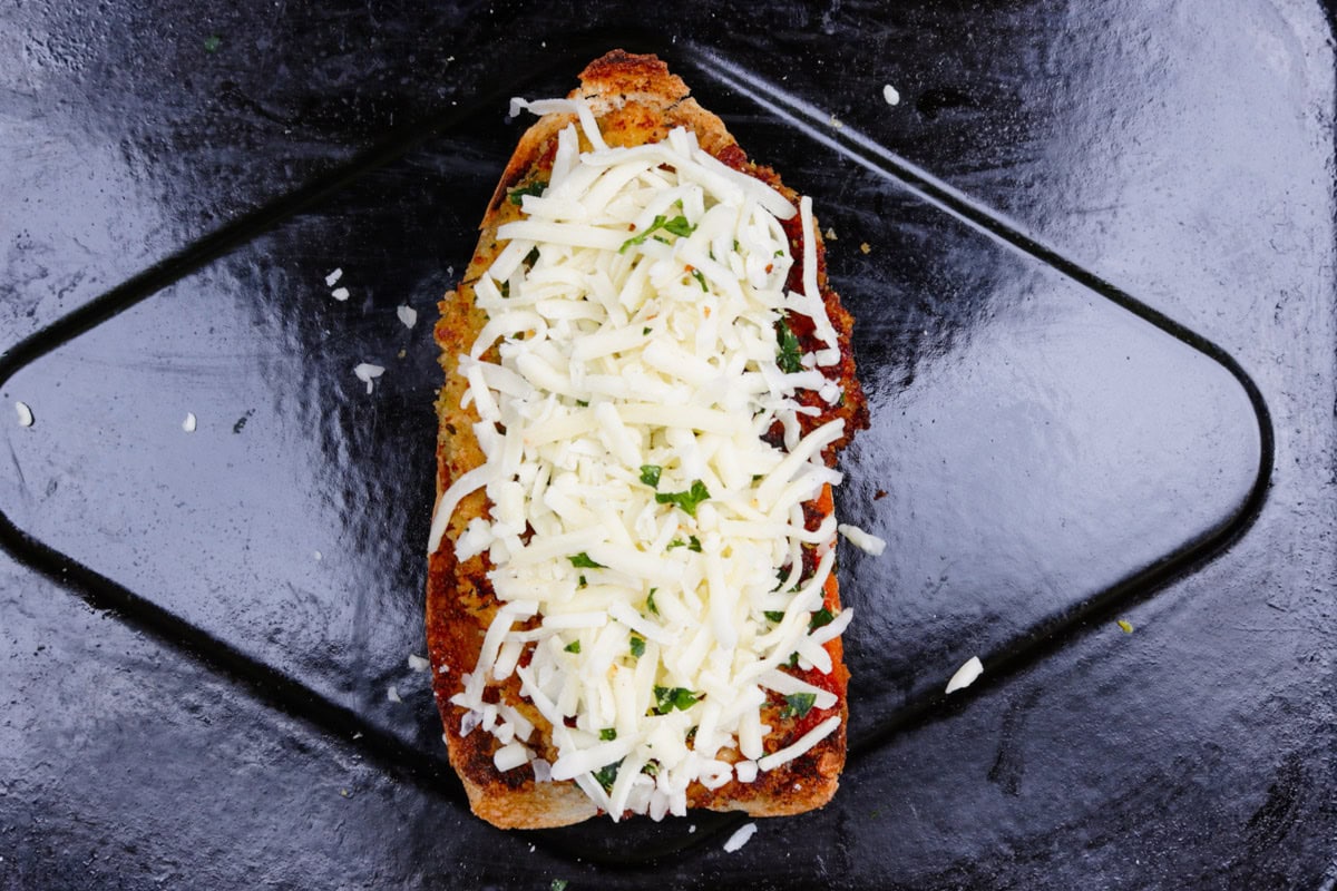 Half toasted roll topped with chicken cutlet and cheese on tray.