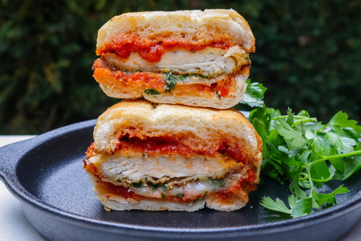 Chicken parmesan sandwich cut in half and stacked on a black plate.