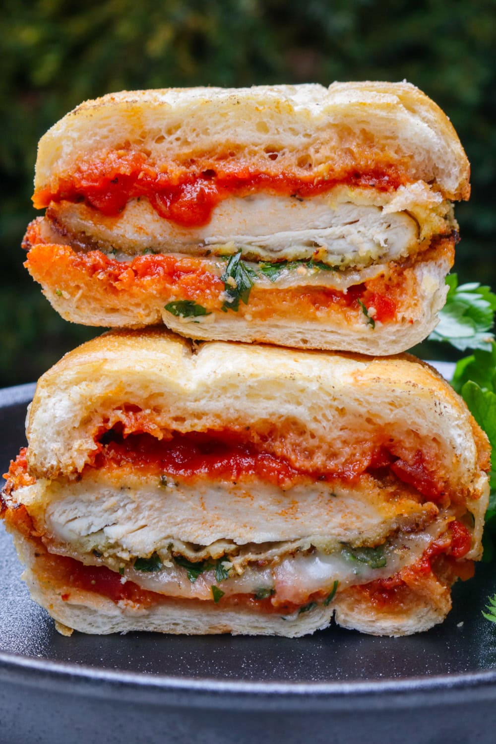 Chicken parmesan sandwich cut in half and stacked on a black plate.