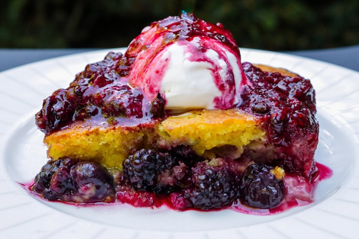 Piece of berry cake topped with vanilla ice cream and berry compote.