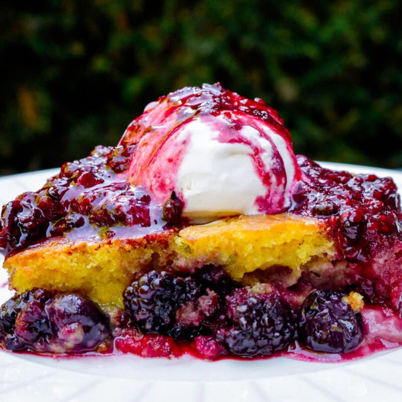Piece of berry cake topped with vanilla ice cream and berry compote.